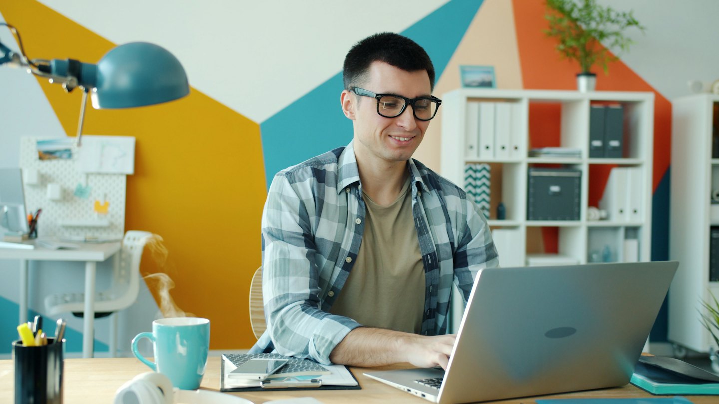 Hombre con gafas trabajando en un portátil en un escritorio.
